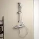Brausethermostat mit Handbrause und Halterung, an einer Wand befestigt. Die Chrom-Oberfläche gehört zur Marke Ideal Standard. In der Nähe ist ein offenes Regal sichtbar.